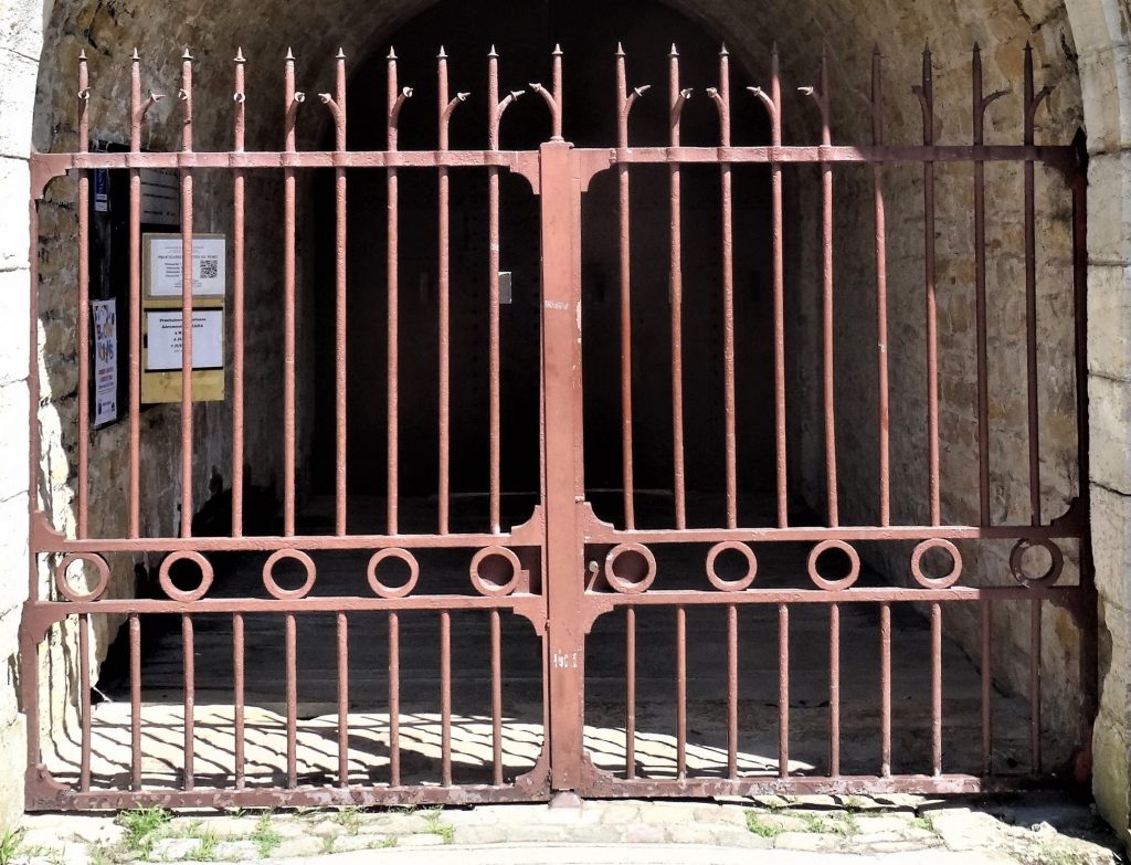 La grille de couleur rouge brique de l'entrée.  Les barreaux sont pointus à la partie supérieure. Une frise horizontale constituée de cercles décore la partie médiane de la grille.